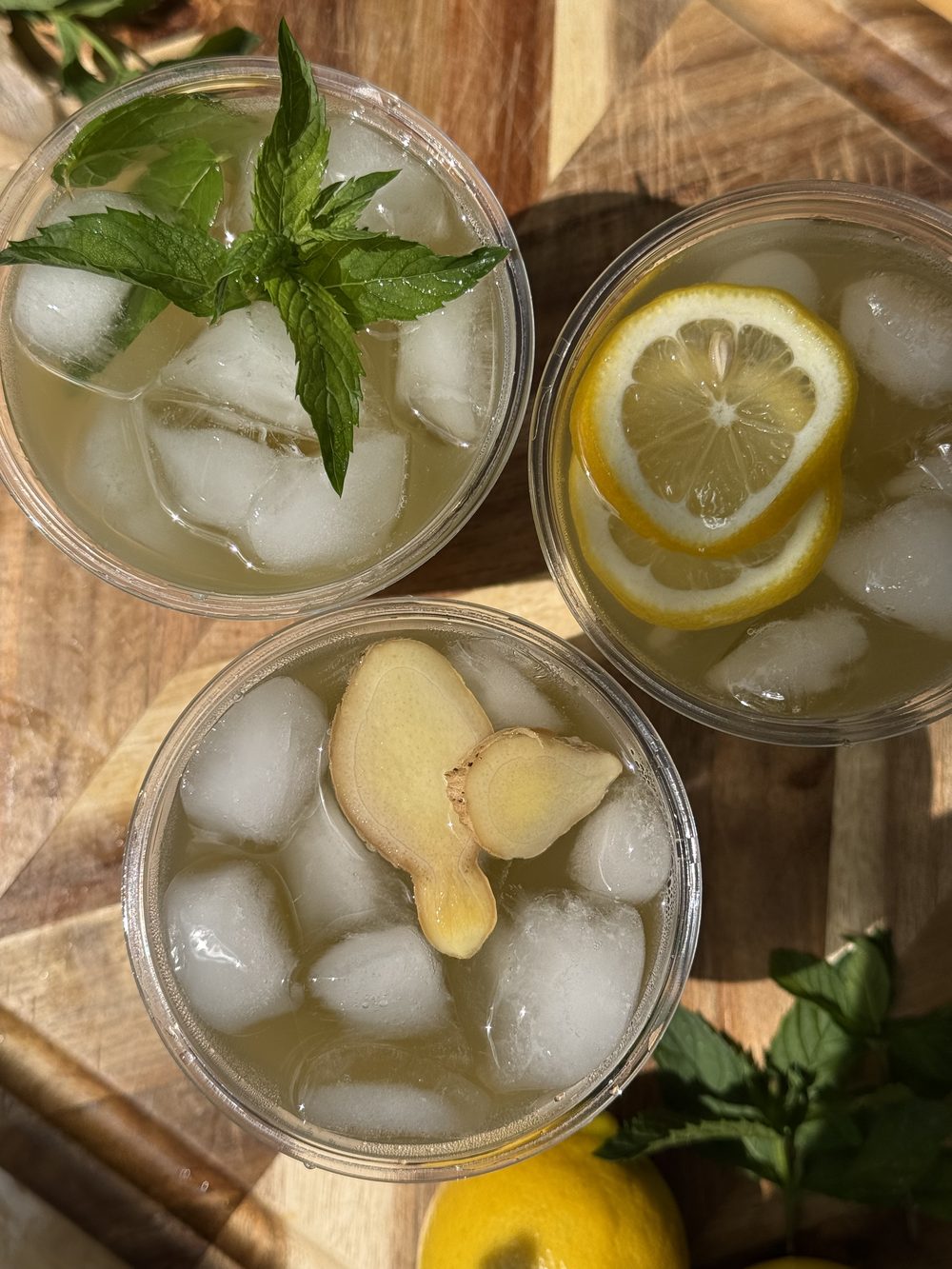 Three cups of iced sugarcane juice garnished with mint, lemon, and ginger